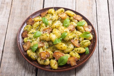 Ahşap arka planda fesleğen, peynir ve mantarlı ev yapımı patates gnocchi.