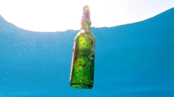 丢弃的玻璃瓶在阳光下缓缓地漂浮在蓝色的水面下 — 图库照片