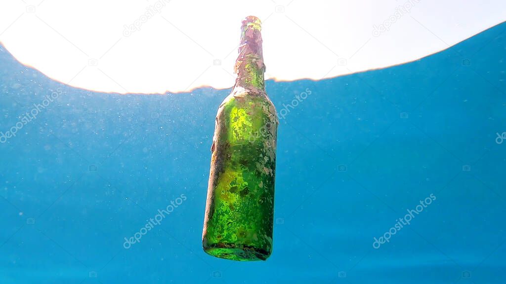 Discarded glass bottle slowly drifting under surface of blue water in sunlight