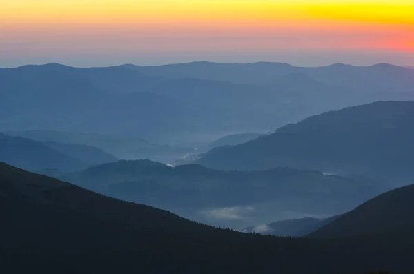 Mountains silhouettes against red and yellow sunrise sky. Little fog is visible in the middle of composition.
