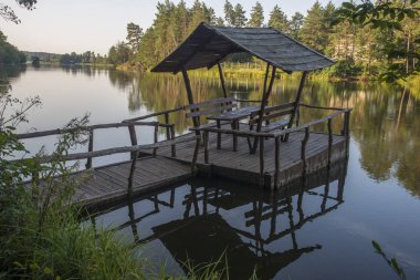 Orman gölü üzerinde bankları ve gölgelikleri olan ahşap bir masa.