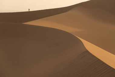 Kum tepeleri yakın çekim ve küçük bir yürüyen adam figürü 
