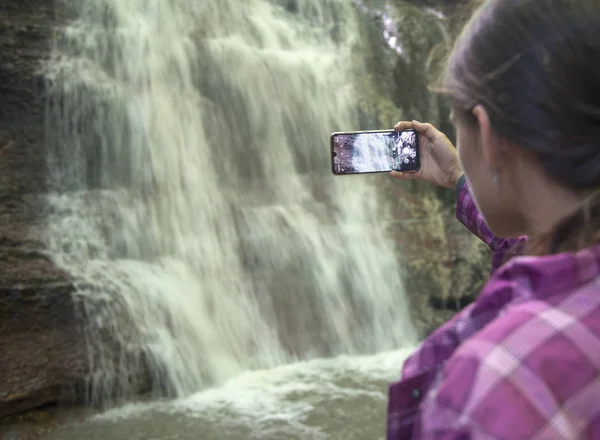 Girl photographs waterfall with smartphone — Stock Photo, Image