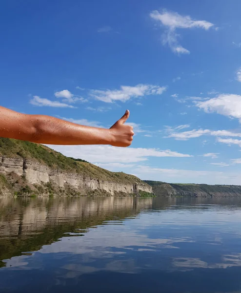 親指を上げて手が旅行が素晴らしいことを示しています 背景には岩や水のある風景 — ストック写真