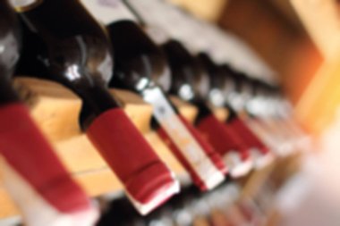 Bulanık kırmızı şarap şişeleri ahşap raflar üzerinde yığılmış