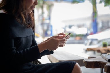 Güzel, genç Asyalı bir kadın kafeteryada ve restoranda internet üzerinden akıllı telefon kullanıyor.