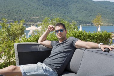Deniz manzaralı bir bahçede kanepede rahatlatıcı yakışıklı genç adam. yaz tatili