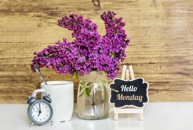 Lila Çalarsaat, fincan kahve ve ahşap arka plan üzerinde Merhaba Pazartesi metin ile buket. Bahar sabah kavramı