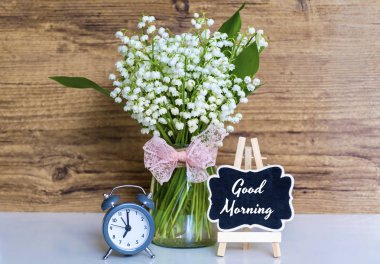 Bir buket Lily vadi çalar saat, fincan kahve ve Günaydın metin ahşap arka planda. Bahar sabahı konsepti