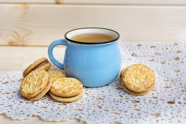 blue mug of tea and sandwich cookies on wooden background