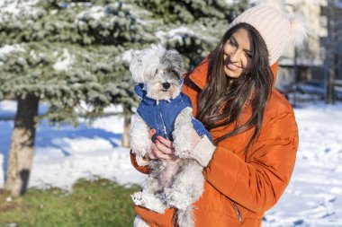 Güzel bir kadın kış ormanında sevimli köpeğini kucaklıyor. Evcil hayvan ve açık hava sahibi.
