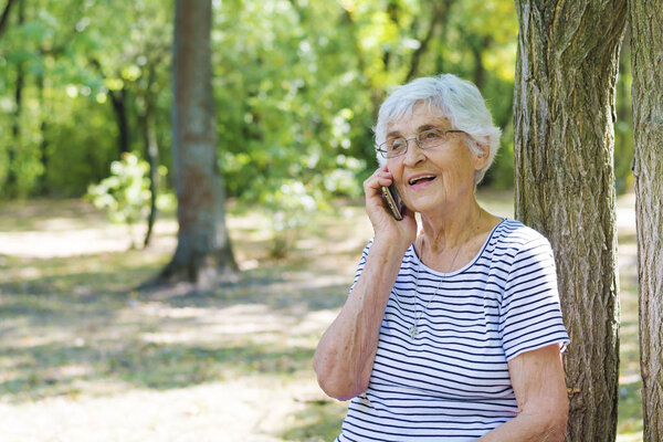 Happy Senior Woman Talking on the  Phone Outdoor in a Green Park