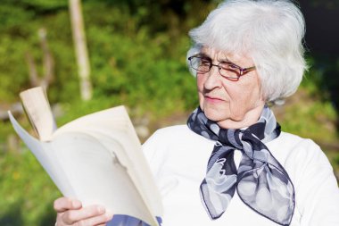 Güzel kıdemli kadın okuma köpeğini bir yaz bahçesinde bir kitapla 