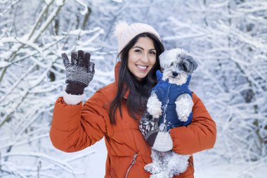 Güzel bir kadın kış ormanında sevimli köpeğini kucaklıyor. Evcil hayvan ve açık hava sahibi.