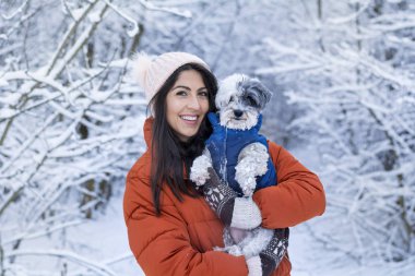 Güzel bir kadın kış ormanında sevimli köpeğini kucaklıyor. Evcil hayvan ve açık hava sahibi.