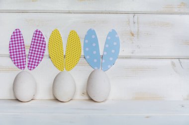 Beyaz ahşap zemin üzerinde kağıt tavşan kulaklı Paskalya yumurtaları