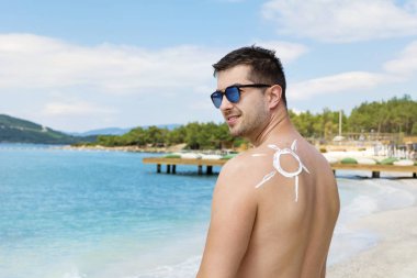 adam güneş şeklinde güneş kremi ile gülümseyen. Güneş çizilmiş üzerinde adam omuz ile güneş koruma kremi