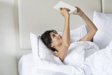 Genç kadın gözler için yanlış pozisyonda yatakta kitap okumak