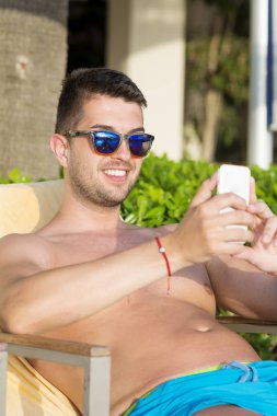 Akıllı telefon kullanarak güneş gözlüğü genç erkek dinlenme 