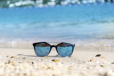 Fashion blue sunglasses on sandy  beach near the blue sea. Summer holiday concept