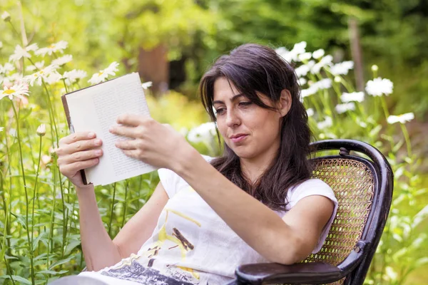 女性は緑の夏の庭で本を読んで — ストック写真