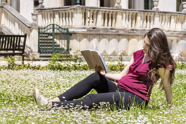若いです妊娠中の女性読書上の草で公園 — ストック写真