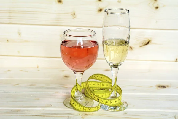 glasses of wine and champagne with measuring tape.Calories in alcohol are extra-fattening