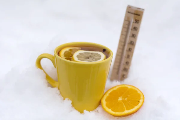 yellow mug of tea with lemon slice and thermometer on the snow