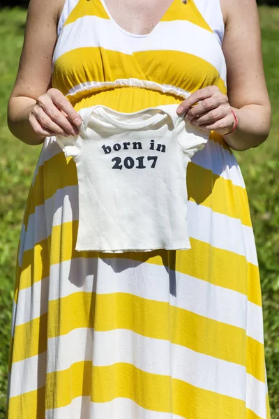 幸せな妊娠中の女性は赤ちゃんの服を保持しています 2017 メッセージを生まれ — ストック写真
