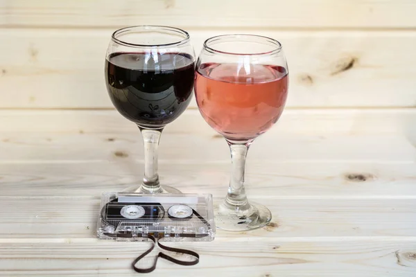 Glasses of red wine , rose and cassette tape isolated on a wooden background. Romantic date concept