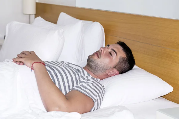 Handsome young man happily sleeping in white bed
