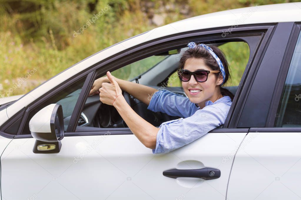 Young happy woman driving new white car and thumbs up