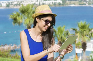 Tablet bir deniz arka plan üzerinde kullanma güzel genç kadın portresi. Yaz tatili