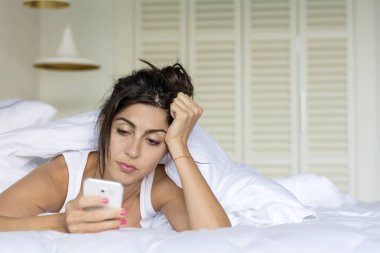Üzgün kadın yatakta telefonda mesaj gönderme