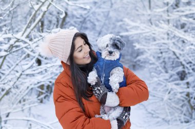 Güzel bir kadın kış ormanında sevimli köpeğini kucaklıyor. Evcil hayvan ve açık hava sahibi.