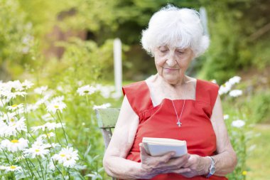 güzel kadın kıdemli bir kitap okuma ve bir bahçede gülüyor 