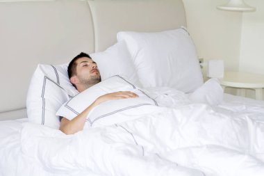 mutlu bir şekilde beyaz yatakta uyuyan yakışıklı genç