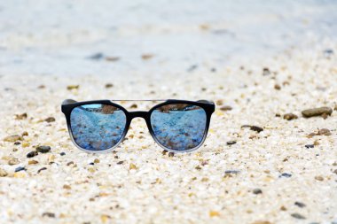 Fashion blue sunglasses on sandy  beach near the blue sea. Summer holiday concept