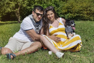 Koca ve hamile karısı yeşil çayırda köpekle piknik yapıyor