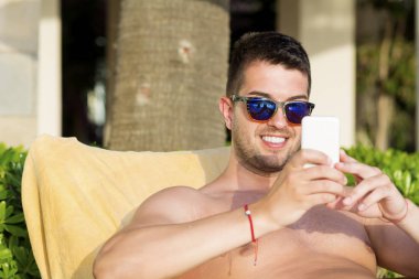 Akıllı telefon kullanarak güneş gözlüğü genç erkek dinlenme 