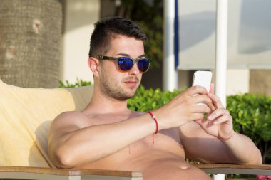 Akıllı telefon kullanarak güneş gözlüğü genç erkek dinlenme 