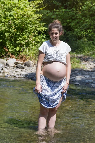 川に立ってブルネットの髪を持つ幸せな妊娠中の女性 — ストック写真