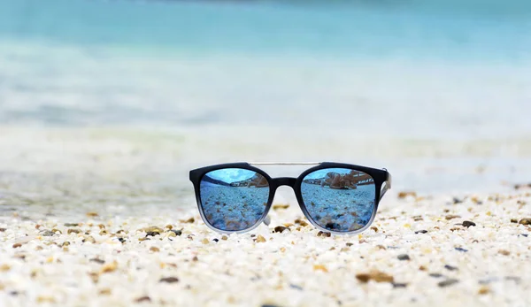 Fashion blue sunglasses on sandy  beach near the blue sea. Summer holiday concept