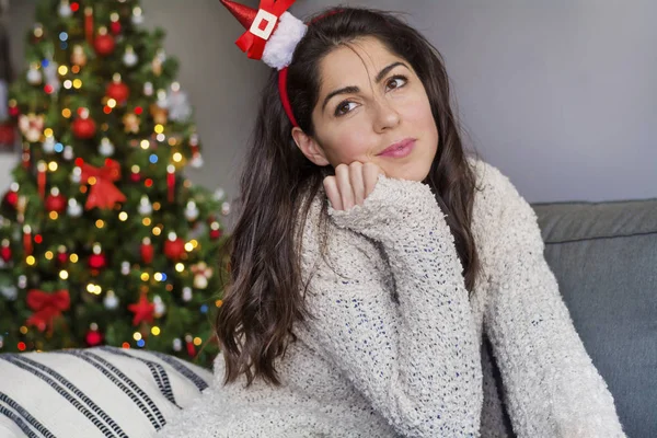 Portrait of beautiful girl in hair band with decor santa hat posing at home