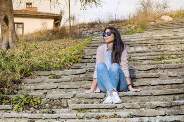 Güzel gülümseyen bir merdivenlerde oturan siyah gözlüklü genç kadın 
