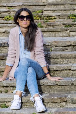 Güzel gülümseyen bir merdivenlerde oturan siyah gözlüklü genç kadın 