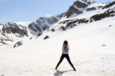 Karlı dağlarda fotoğraf makinesiyle fotoğraf çeken yüzü belirsiz bir kadın.