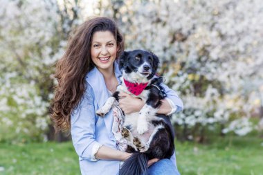 Güzel Gülümseyen Kadın Bir Bahar Bahçesi onu Sevimli Köpek Sarılma . İlkbaharda Evcil Hayvan ve Sahibi Açık