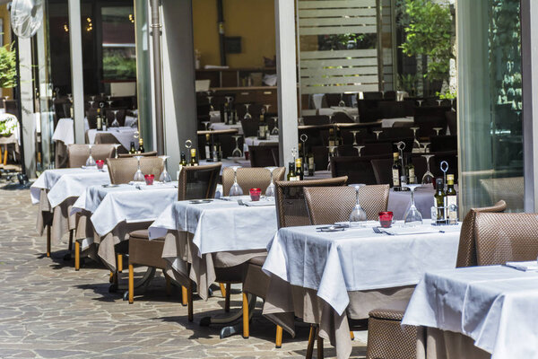COMO, ITALY, JUNE 27, 2018: Cozy Italian Restaurant with White Umbrellas and Tables in a Row on the Street in Italy