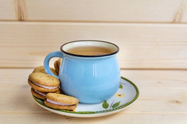 ahşap arka plan üzerinde çay ve sandviç kurabiye mavi kupa 